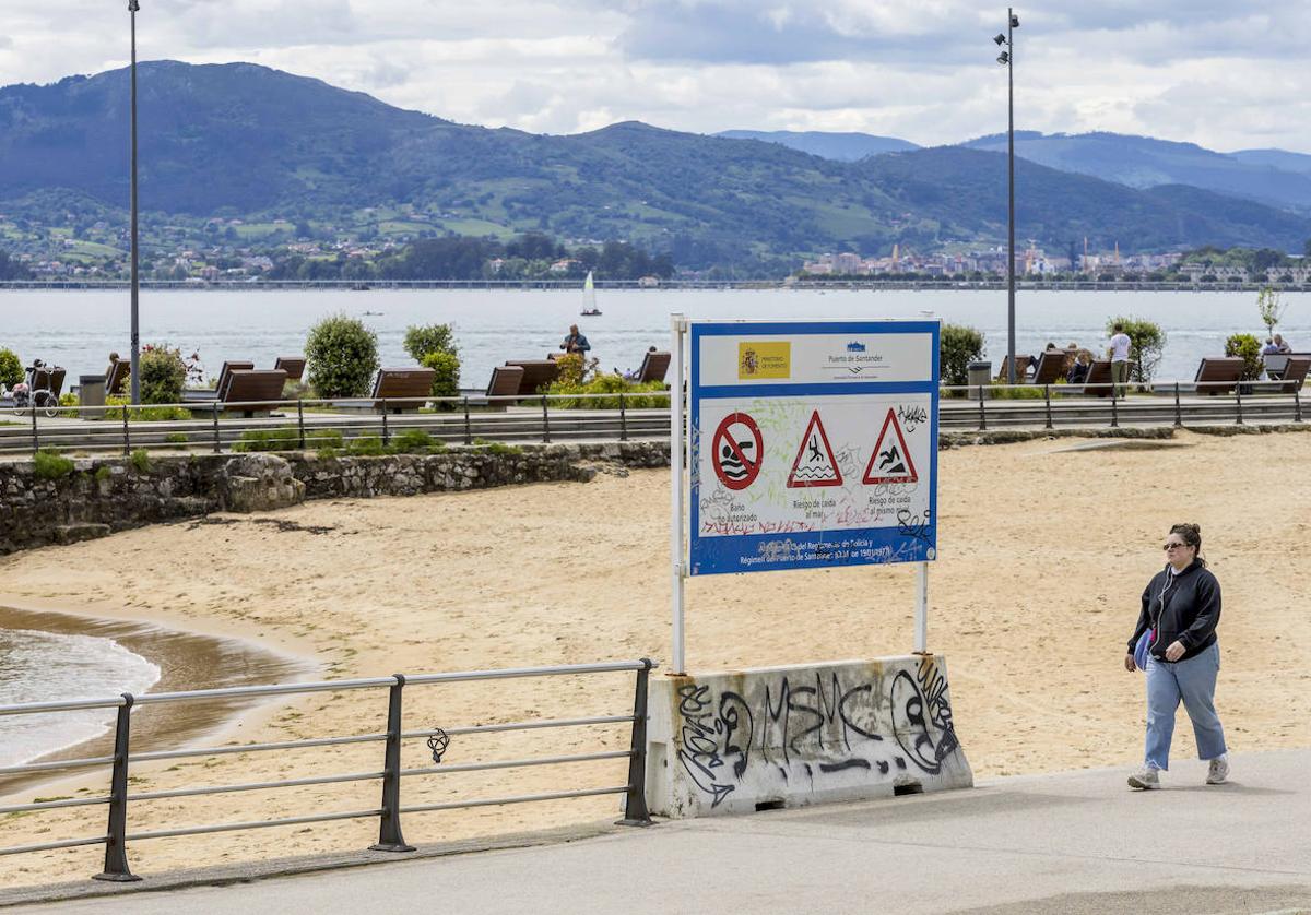 Una mujer pasea junto a la playa que se ha formado en la rampa del Mundial de Vela y el cartel del Puerto que prohibe el baño.