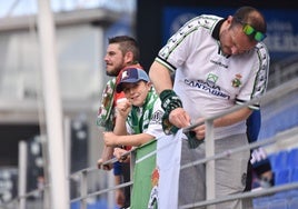 Un aficionado del Racing, junto a su hijo, cuelga una bandera del equipo en la grada