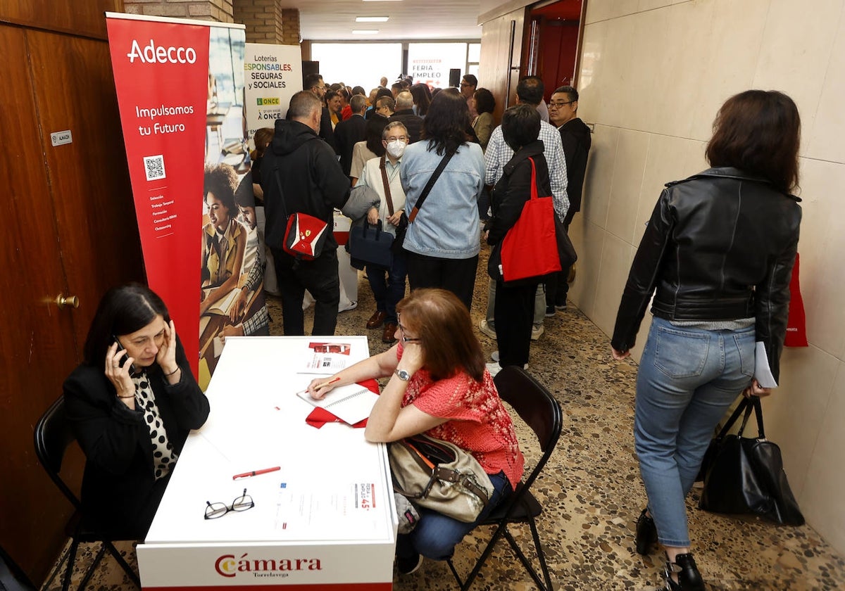 Una vecina recibe asesoramiento en uno de los puestos de la Feria de Empleo 45+, este miércoles, mientras decenas de personas visitan la sede de la Cámara de Torrelavega en el marco de la jornada inaugural.