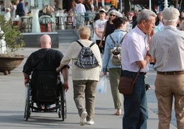 Una mujer acompaña a un hombre en silla de ruedas.