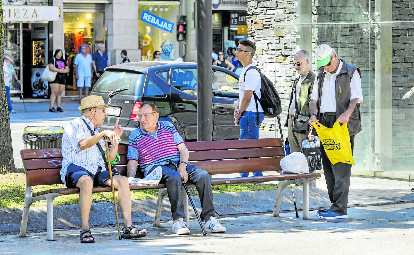 Un grupo de personas mayores descansa en los bancos de la plaza del Ayuntamiento de Santander.