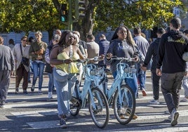 Dos chicas cruzan con bicicletas eléctricas municipales por un paso de cebra del centro de la ciudad.