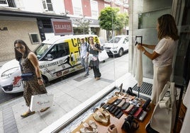 Tres personas miran el escaparate de una tienda de moda en la calle Hernán Cortés, de Santander.