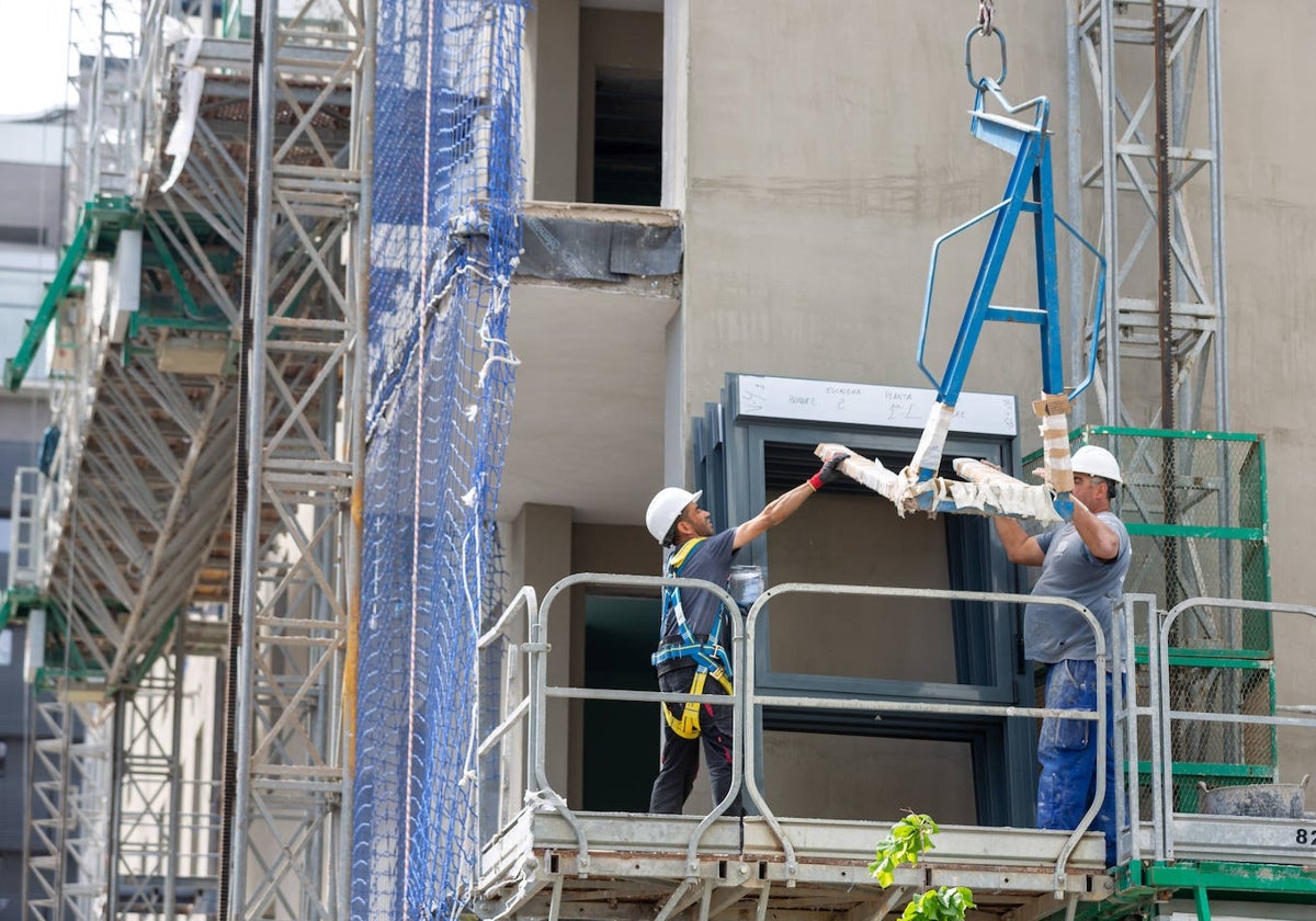 Dos operarios trabajan con una herramienta suspendida de una grúa.