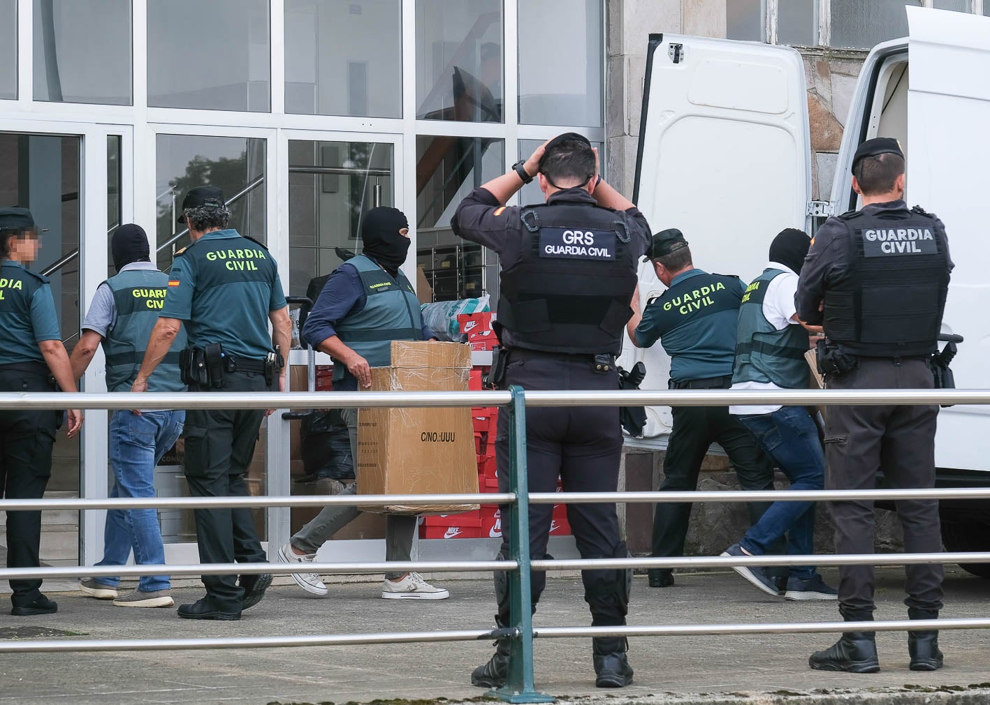 Agentes, algunos encapuchados, depositan en una furgoneta cajas con material incautado en la casa de uno de los detenidos, en Torrelavega.