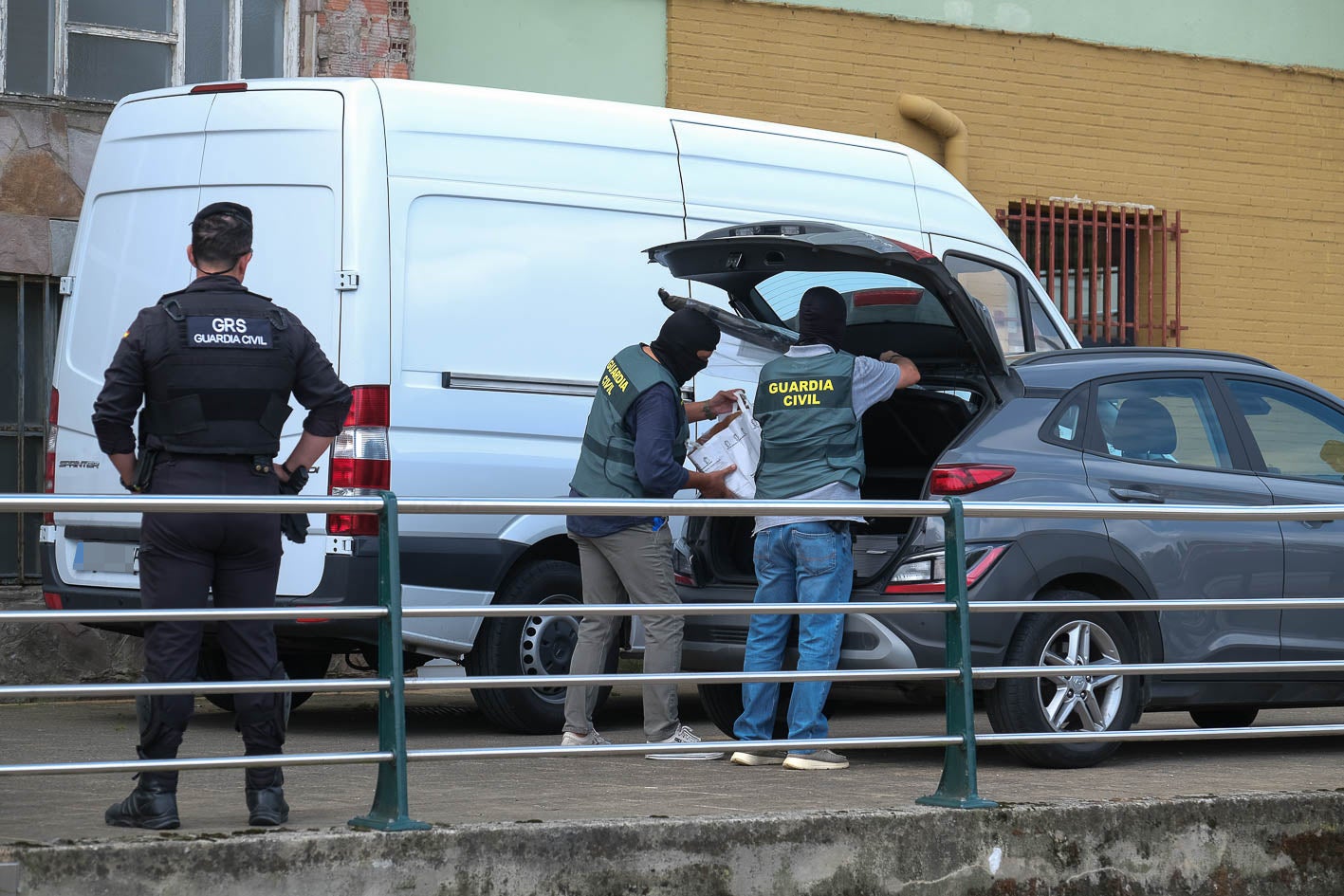 Un agente observa como dos compañeros introducen en el maletero de un coche material incautado.