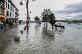 Una persona contemplando cómo estaba San Vicente de la Barquera desde uno de los bancos del Paseo Marítimo inundado en octubre de 2023.