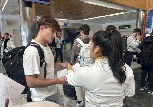 Una de las azafatas de Ryanair entrega una hoja con los derechos de los pasajeros en caso de denegación de embarque a un chico que ha sufrido la cancelación del vuelo París.