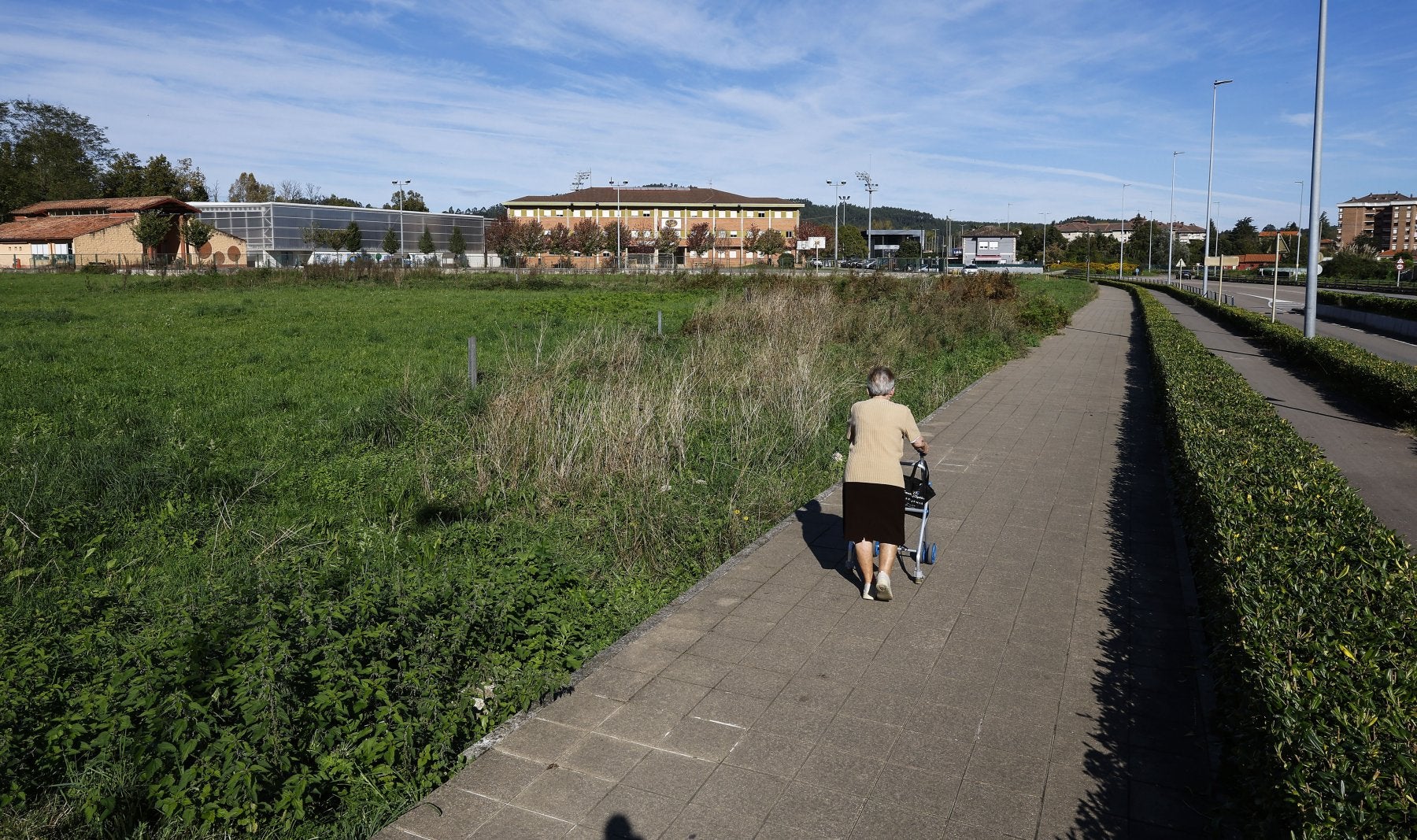 Una vecina camina junto a la zona verde donde se halla la parcela en venta, en Torrelavega.