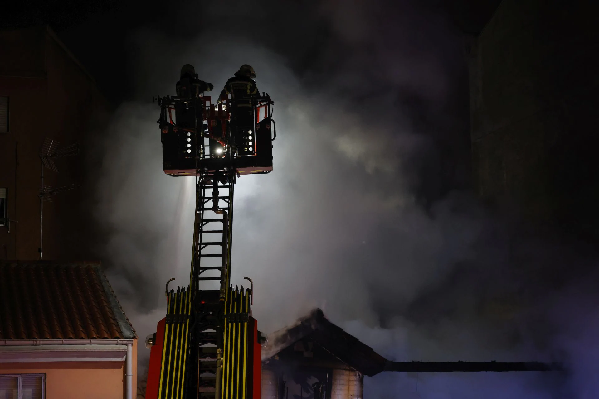 Bomberos en la autoescala atacando las llamas desde lo alto.