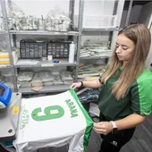 Una de las empleadas de la tienda estampa en una camiseta el nombre y el número de Arana en el cuarto que hay al fondo del establecimiento.