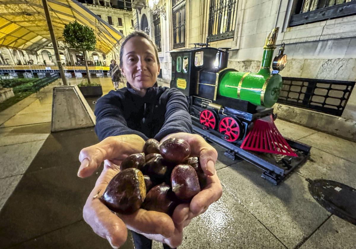 Teresa Salas muestra unas castañas junto a su conocida locomotora en La Porticada.