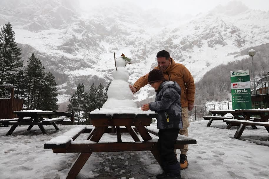 Un niño y su padre hacen un muñeco de nieve cerca de la estación del teleférico de Fuente Dé.