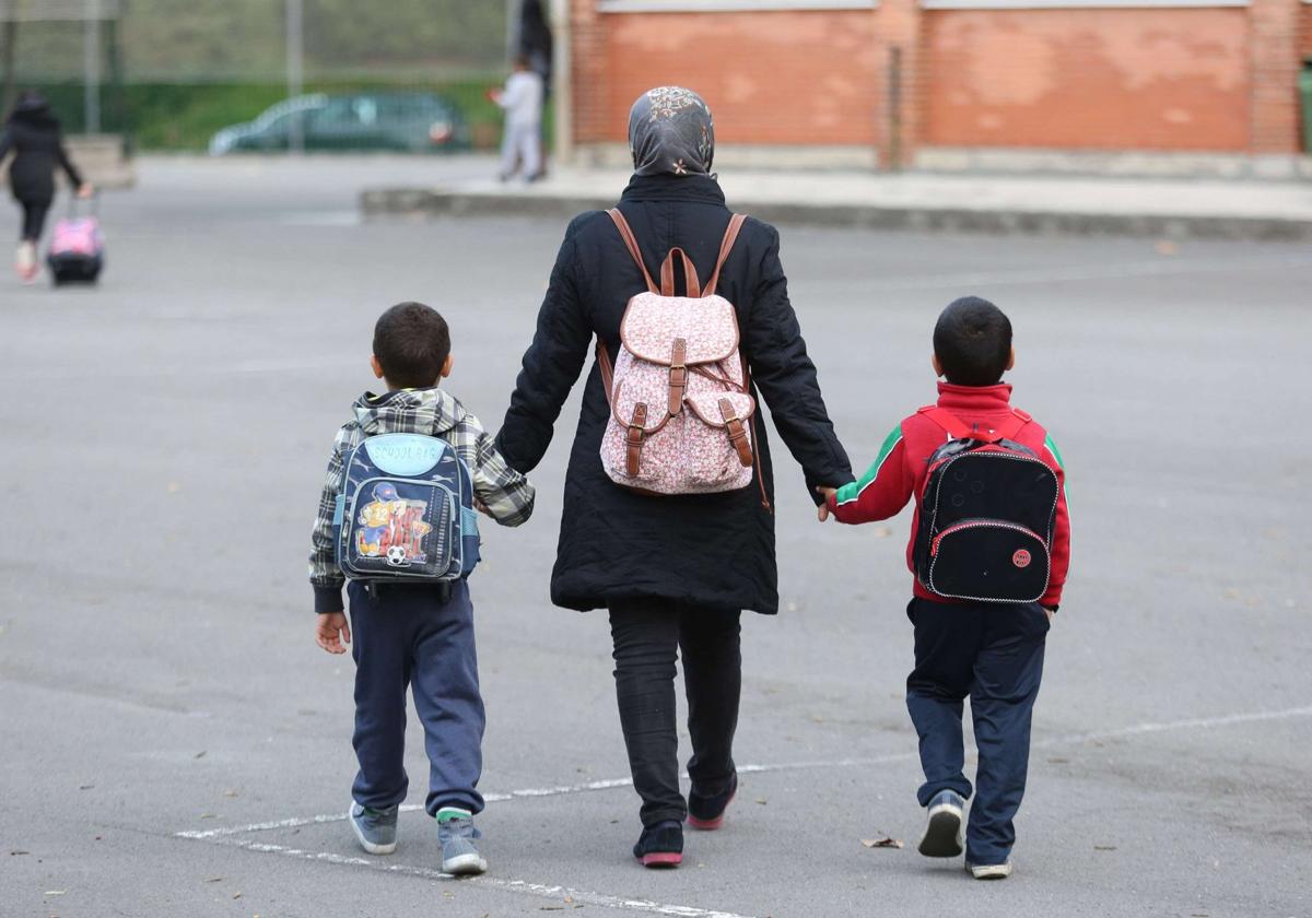 Una mujer extranjera acompaña de la mano a dos niños al colegio.