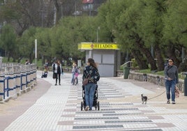 Una mujer pasea por El Sardinero portando un silla infantil, con varios niños y niñas jugando al fondo.