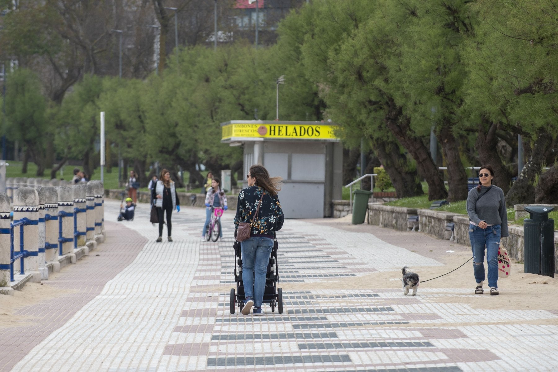 Una mujer pasea por El Sardinero portando un silla infantil, con varios niños y niñas jugando al fondo.