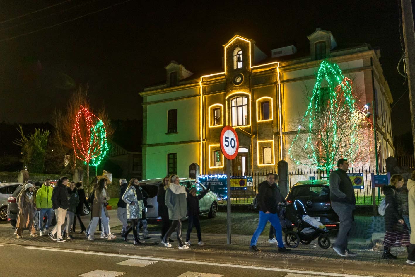 Varias personas atraviesan la recta con los edificios iluminados.