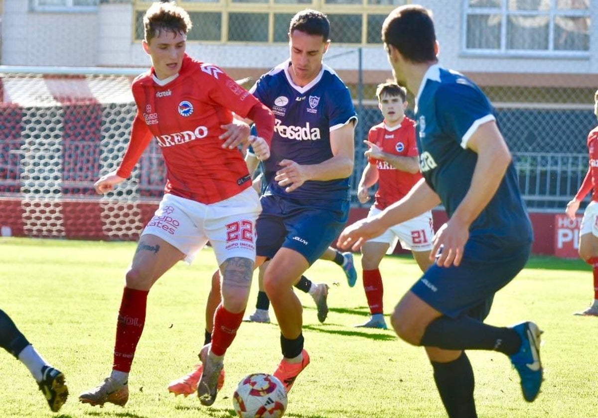 Un jugador del Laredo pugna con dos rivales del Marino de Luanco por hacerse con la pelota