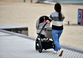 Una madre pasea junto a su bebé cerca de la playa.