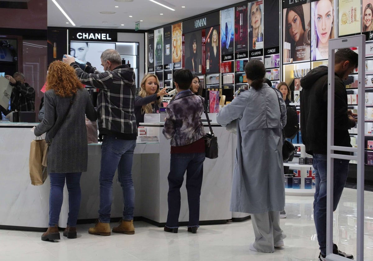 Una dependienta atiende a varios clientes en un establecimiento de cosmética.