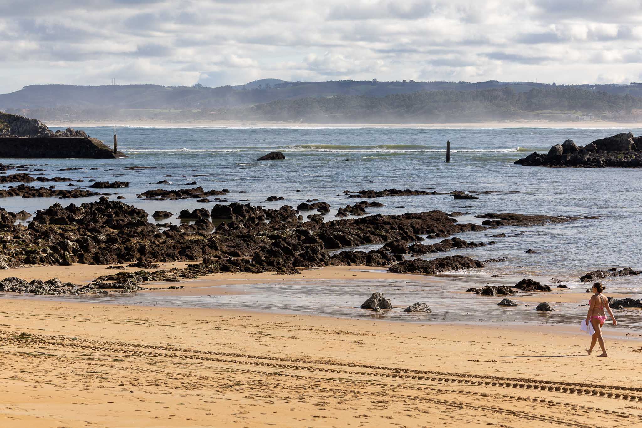 Una mujer pasea por la playa de Los Bikinis, mientras que en el firme se ve el paso de una grúa que adencentaba el arenal tras los desperfectos ocasionados por el temporal.