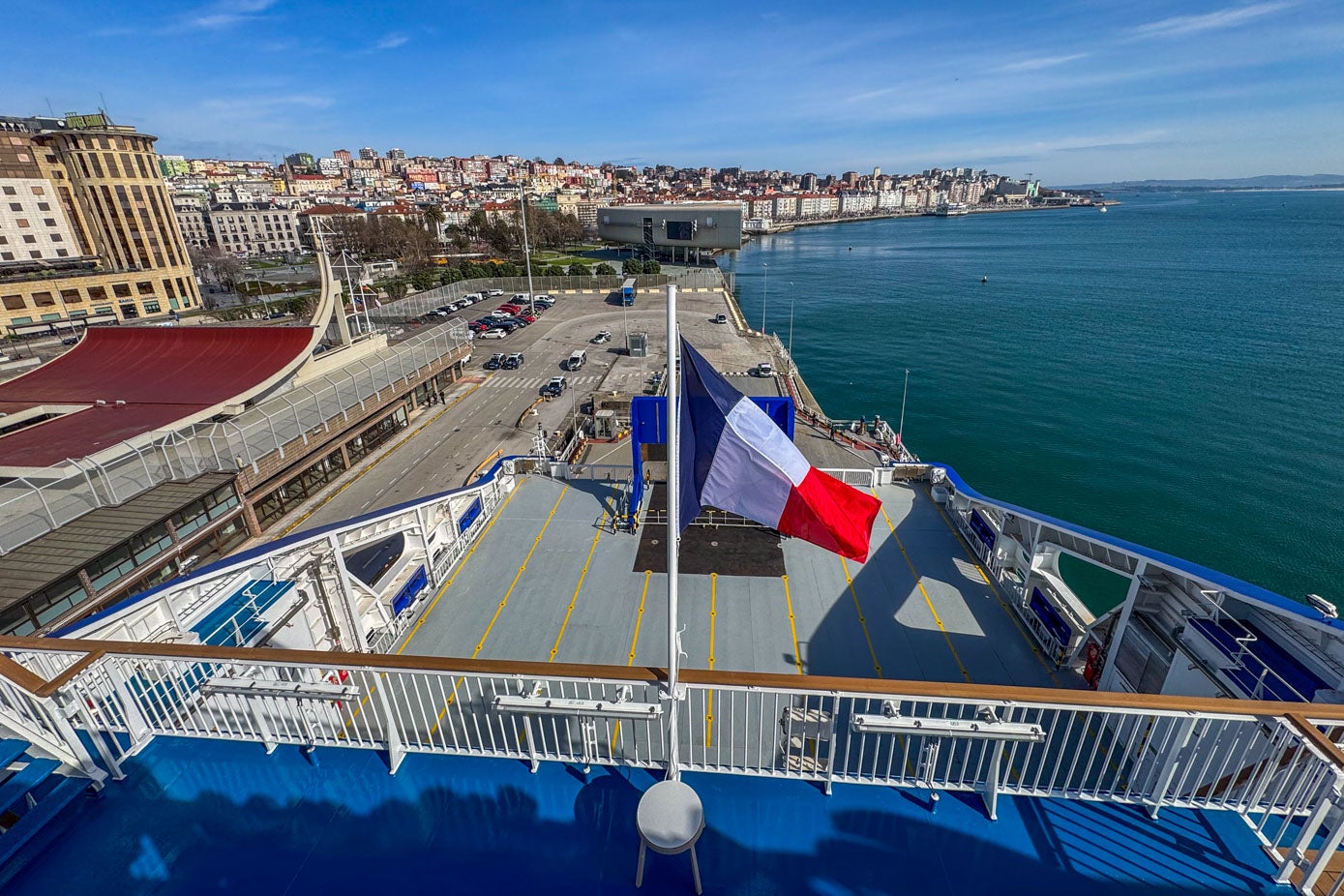 La bandera, ya izada, con los muelles del puerto, la bahía y el Centro Botín al fondo.