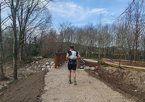 Un joven atraviesa una de las pasarelas de madera que se han instalado en la senda que discurre paralela al río Saja.