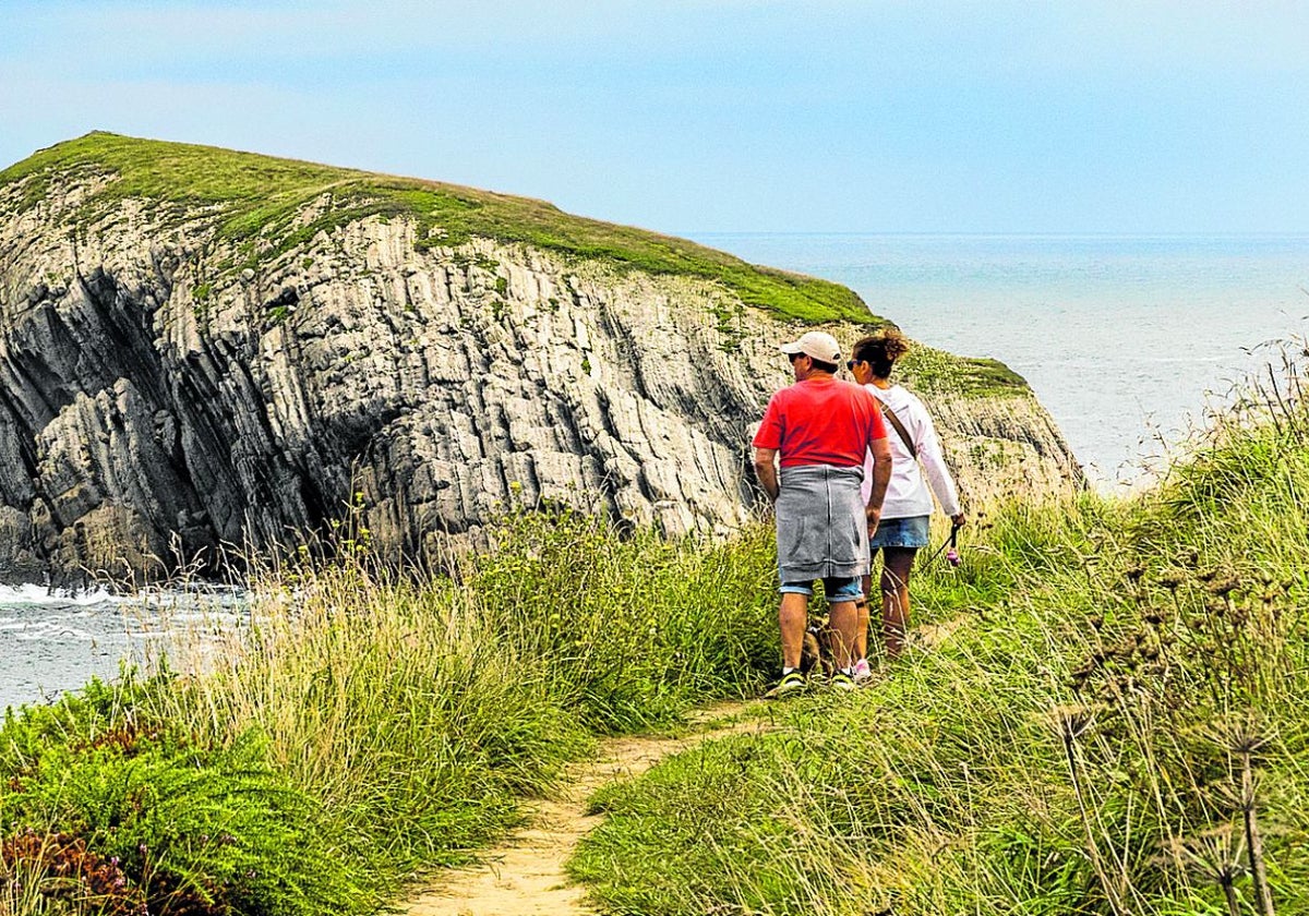 Dos turistas caminan por el sendero que conduce a la playa de Covachos, en el municipio de Santa Cruz de Bezana.