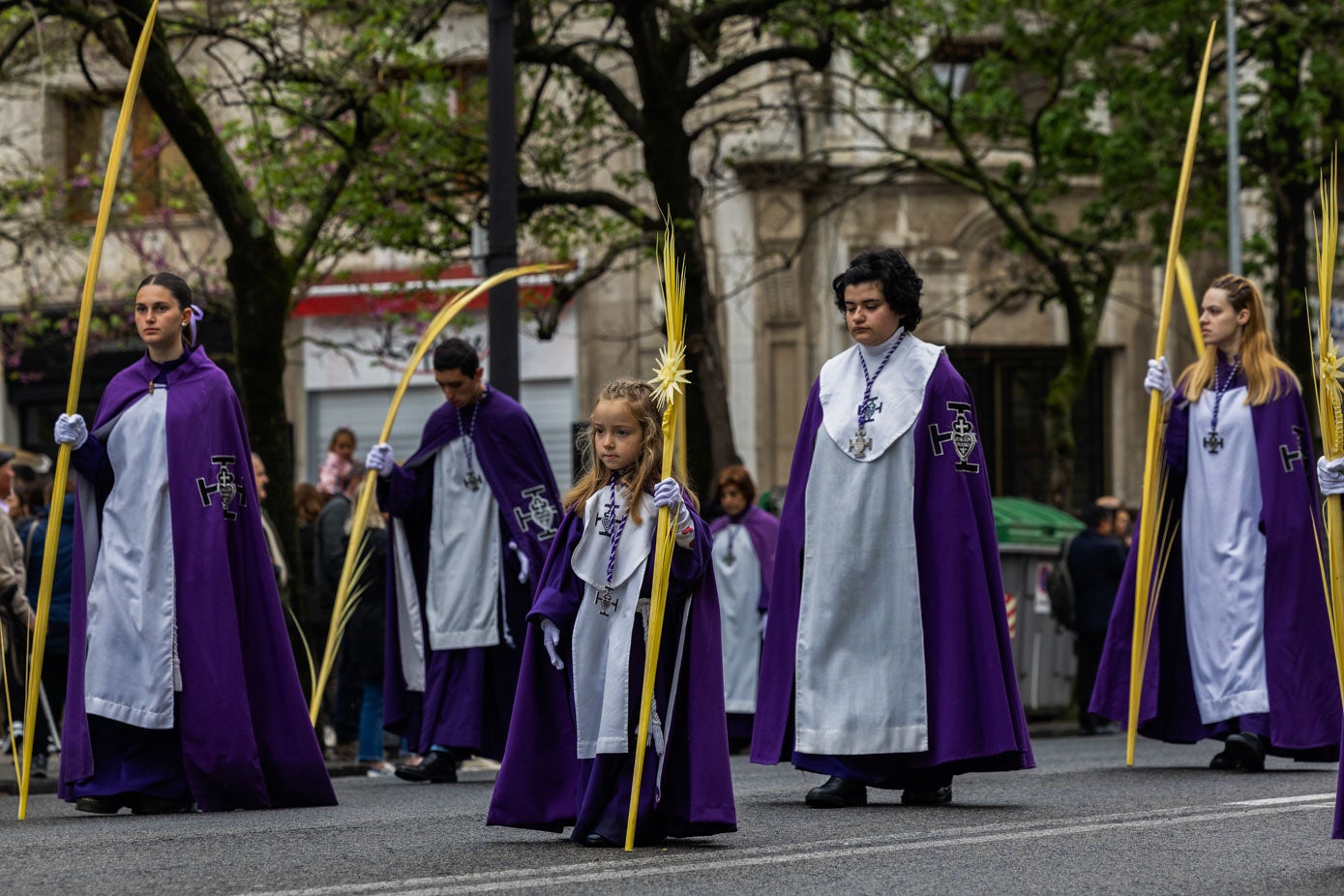 Una niña participa en la procesión con compañeras más mayores portando las hojas de palma