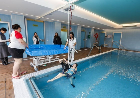 La fisioterapeuta Inés del Río sostiene y ayuda a una usuaria, Nuria, a salir del agua con un arnés, en la piscina terapéutica.