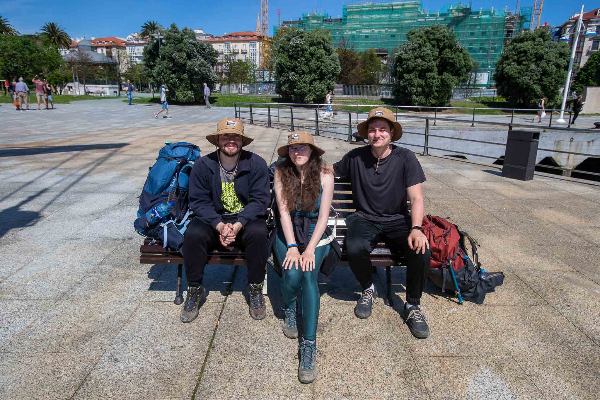 Peregrinos protegidos del sol con sombreros descansan en un banco en el centro de Santander