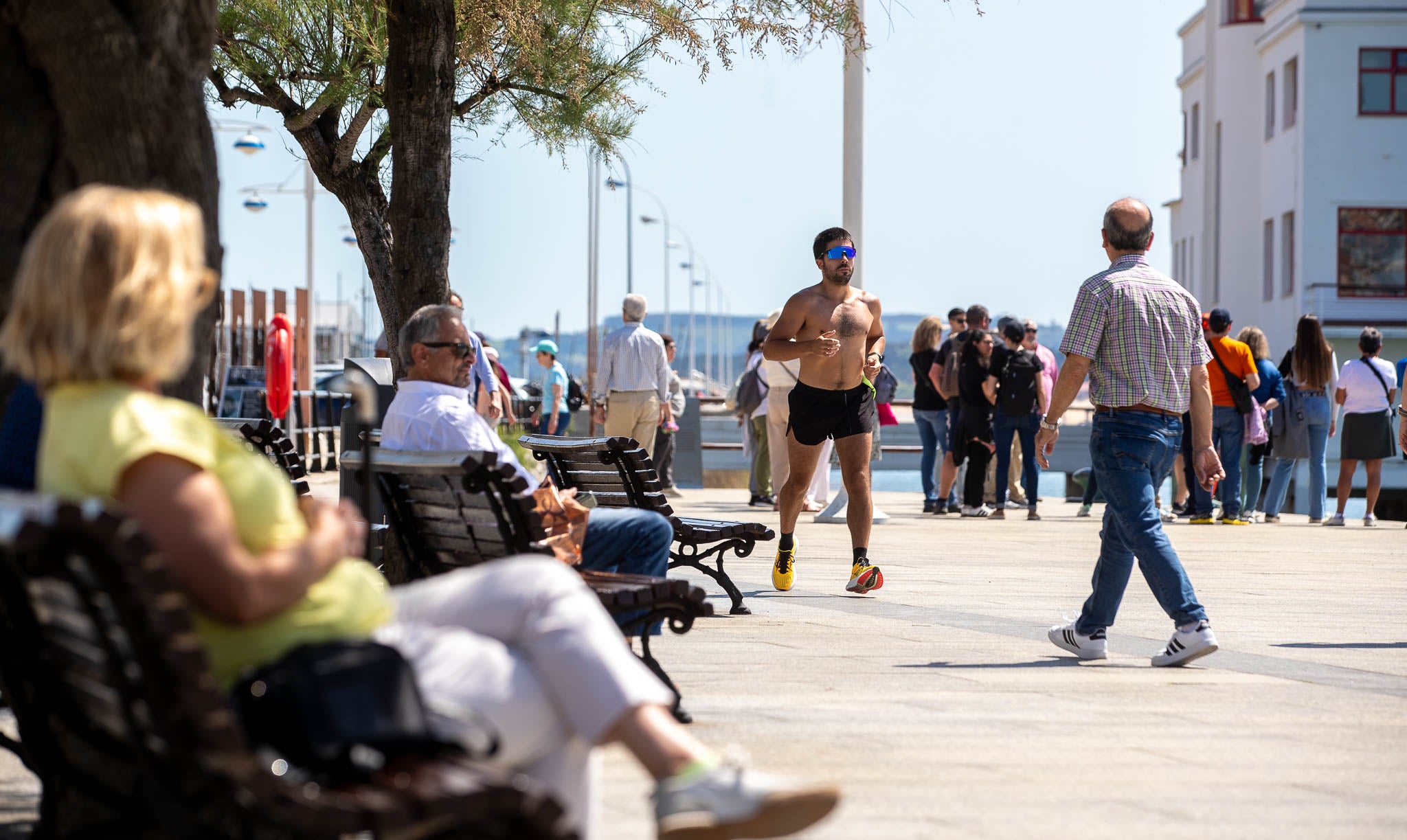 Deportista corre a pecho descubierto por un paseo marítimo lleno de gente