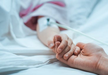 Un familiar sostiene la mano de un paciente en cuidados paliativos.