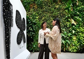 Odette Álvarez explica a la alcaldesa de Santander que con el vestido negro de abalorios expuesto en la pared, acompañado de unas alas confeccionadas en colaboración con Farid Joyeros, desfiló por primera vez en la Mercedes-Benz Fashion Week Madrid.