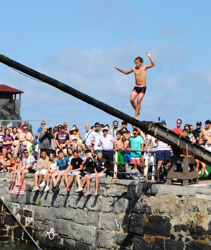 Imagen secundaria 2 - Un joven intenta cruzar la cucaña desde un muelle abarrotado de público expectante y grupos de niños y familias en la merienda de San Pelayo.