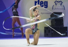 Una gimnasta dibuja con su cinta en plena actuación sobre el tapiz del Palacio de los Deportes. Manejos con mazas sobre el suelo.