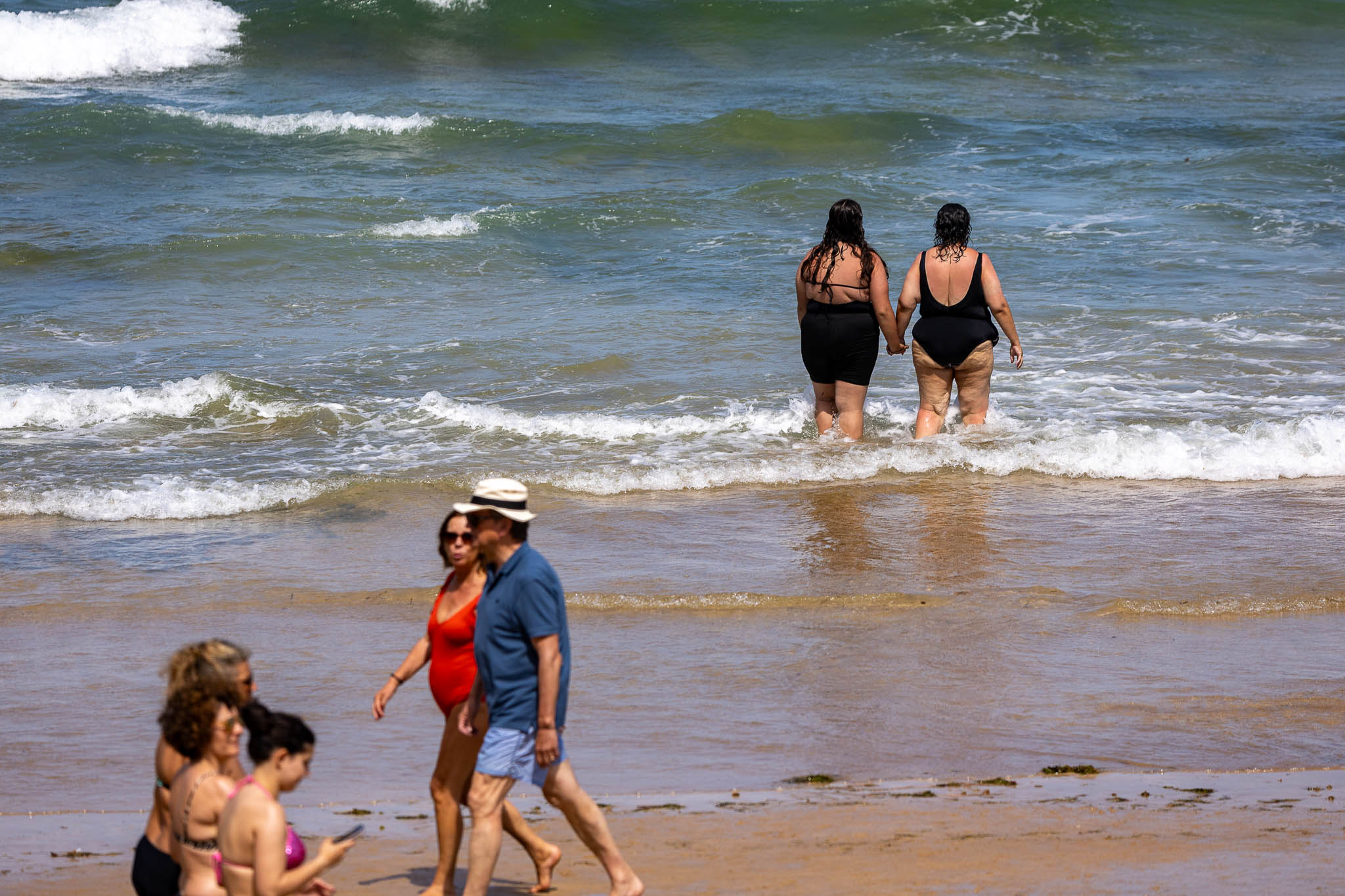 Una pareja pasea mientras dos chicas se bañan.