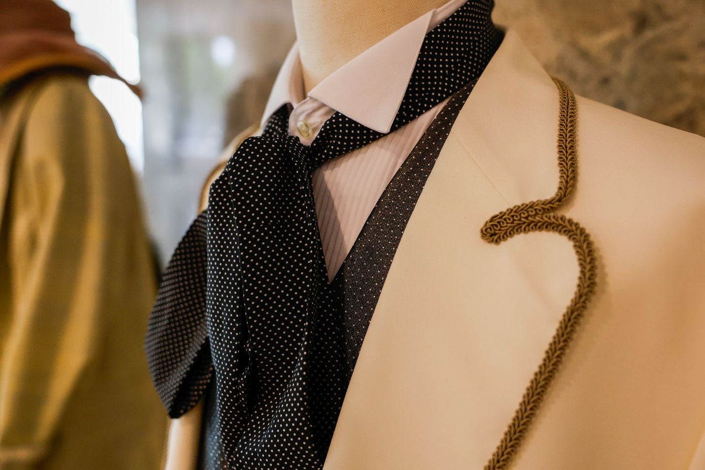 Detalle de la lazada al cuello forrada en pequeños lunares del traje de caballero, así como del ribete de pasamanería confeccionado a mano por la modista.