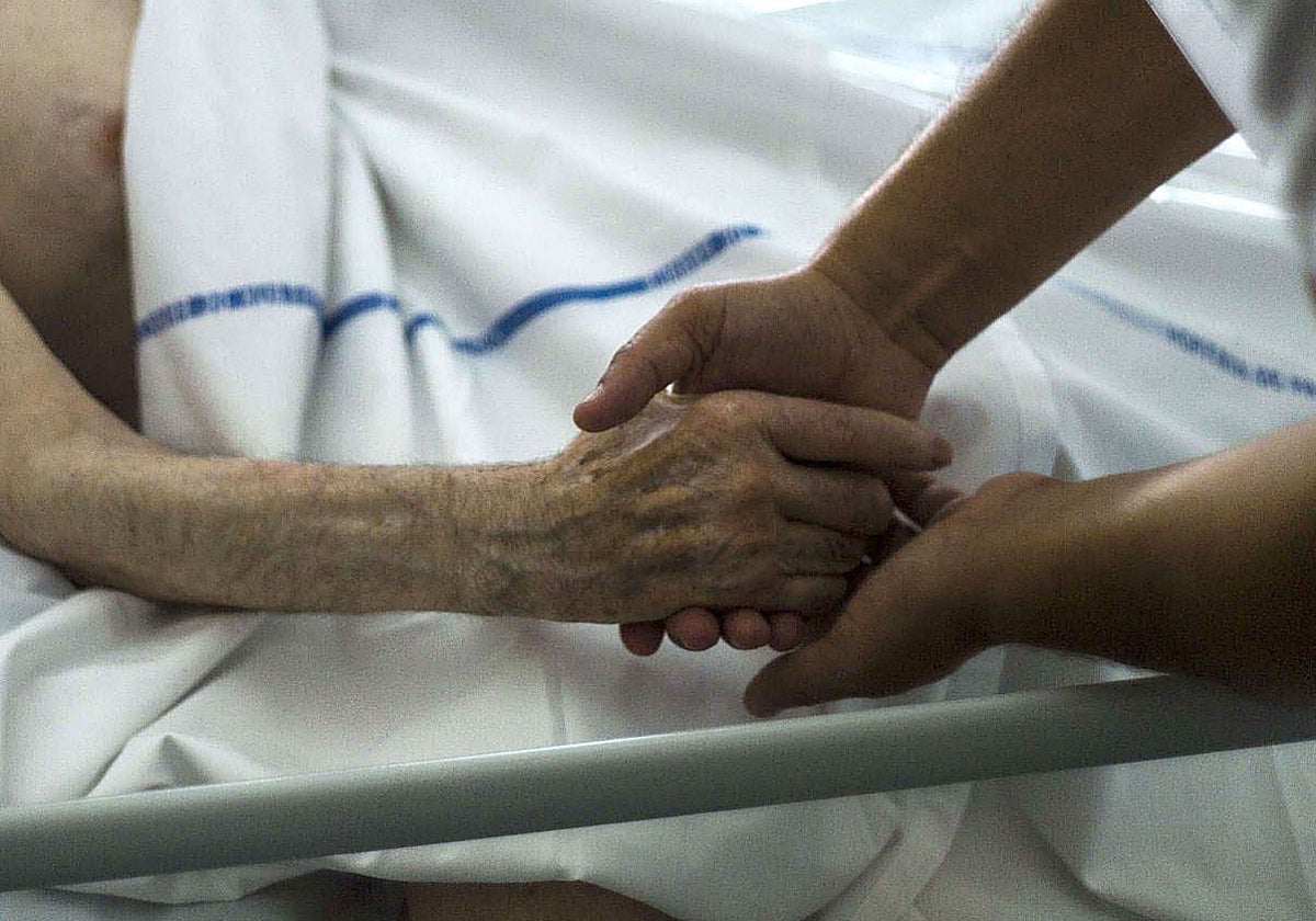 Un paciente agarra su mano a la de un profesional que le atiende al final de su vida.