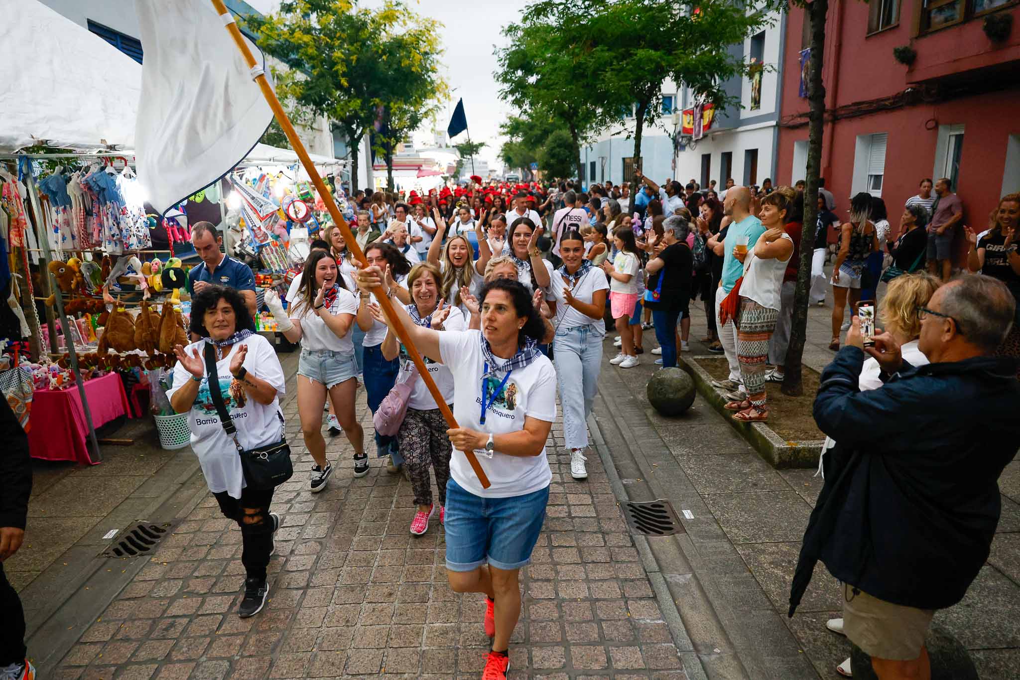 El pasacalles hacia la plaza por la calle principal del barrio, llena estos días de puestos.