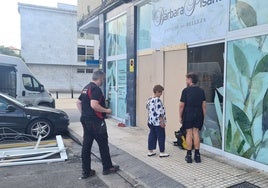 Vecinos se interesan por el estado del escaparate del negocio, junto a uno de los profesionales que lo reparó, este viernes, en la calle Pintor Varela de Torrelavega.