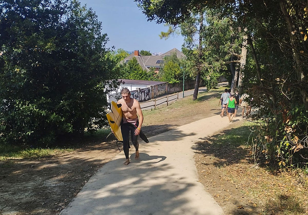 Un joven atraviesa la senda del Monte Ara de Somo con una tabla de surf.