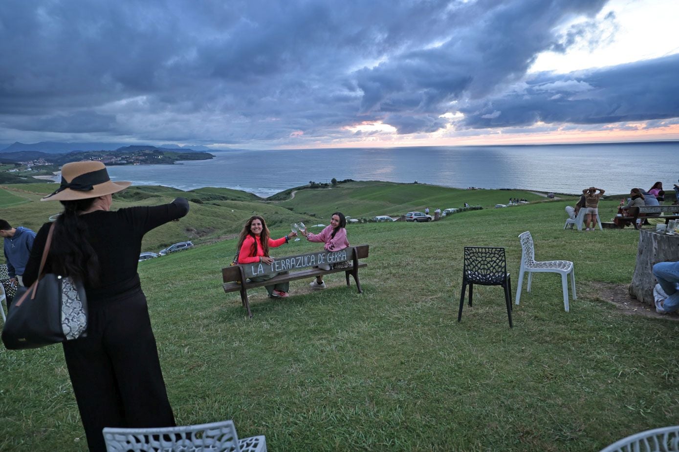 Dos chicas brindan en un banco con vistas al mar.