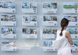 Una mujer mira anuncios de venta de viviendas en el escaparate de una agencia inmobiliaria.