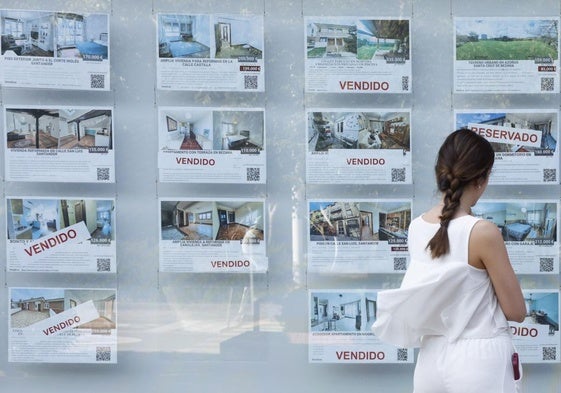 Una mujer mira anuncios de venta de viviendas en el escaparate de una agencia inmobiliaria.