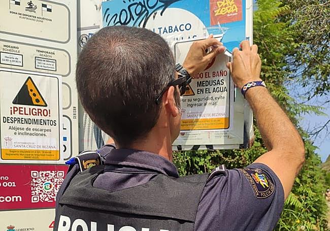 Un policía quita un falso anuncio institucional de un cartel en la playa