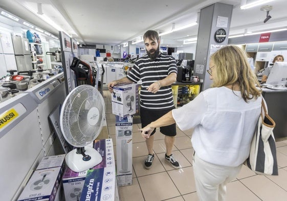 José Mayoral, vendedor en Electrodomésticos J. Rivero, muestra algunos de los ventiladores que le quedan en la tienda a una clienta.