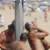 Personas duchándose en la playa a primera hora de este viernes.