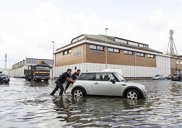 Dos hombres intentan ayudar a un conductor a salir de una balsa de agua en el polígono Candina.