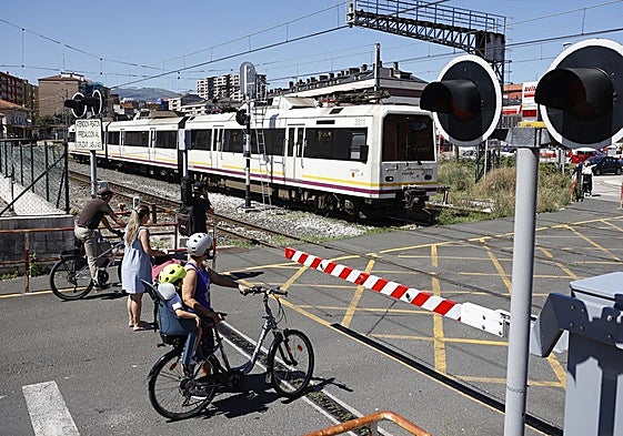 Un tren parte de la estación de Torrelavega mientras vecinos esperan en el paso a nivel de Pablo Garnica, en Torrelavega.
